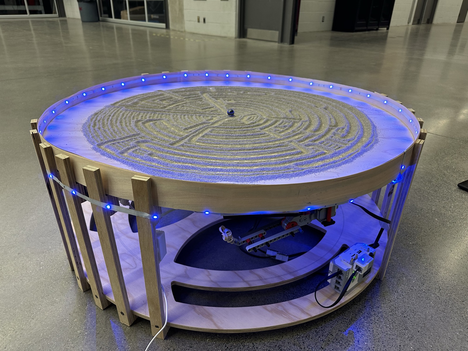 The Atlas Sand Table: a round wooden table with LED-lit rim, sand surface with a drawn maze pattern, and the LEGO EV3 mechanism visible underneath