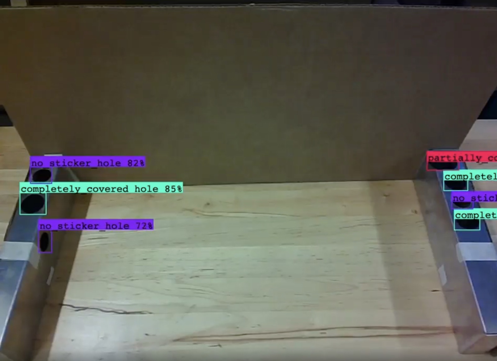 Camera view of two metal rails with detection boxes labeling holes as no sticker, completely covered, or partially covered, with confidence scores